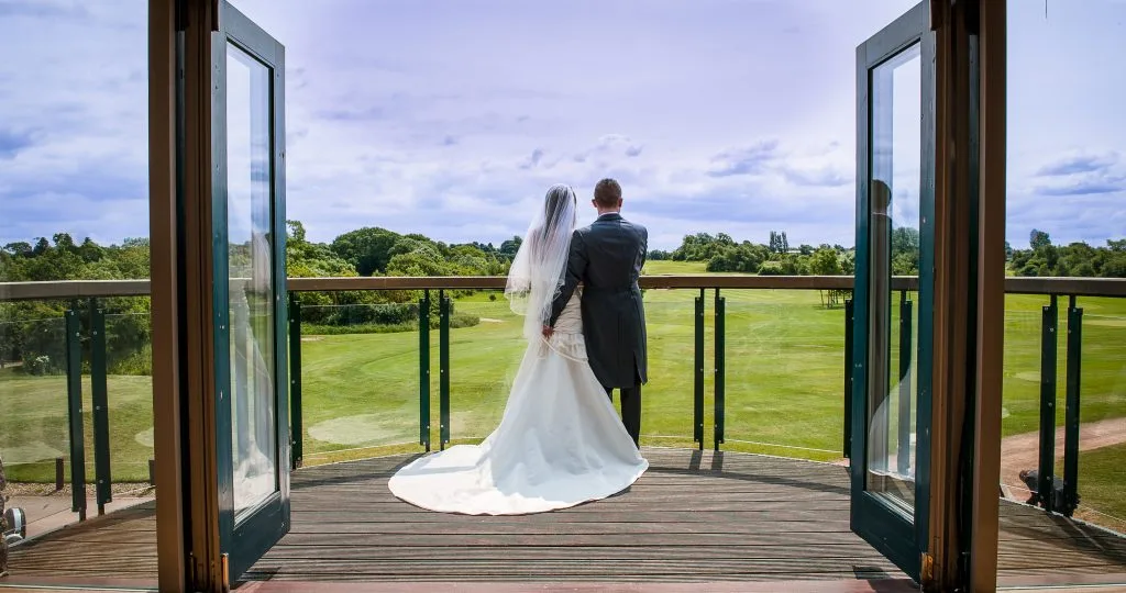 Couple standing on a balcony overlooking the golf course at Thornbury Golf and Lodge, a picturesque wedding venue near Bristol