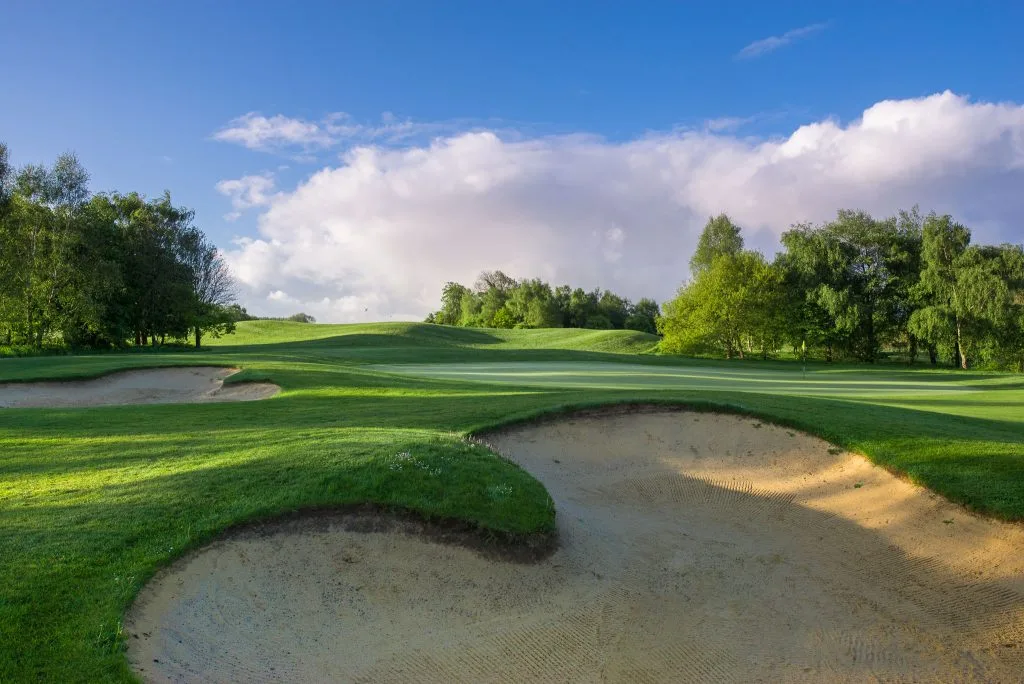 A serene golf course with long shadows stretching across the fairway, golden light filtering through the trees