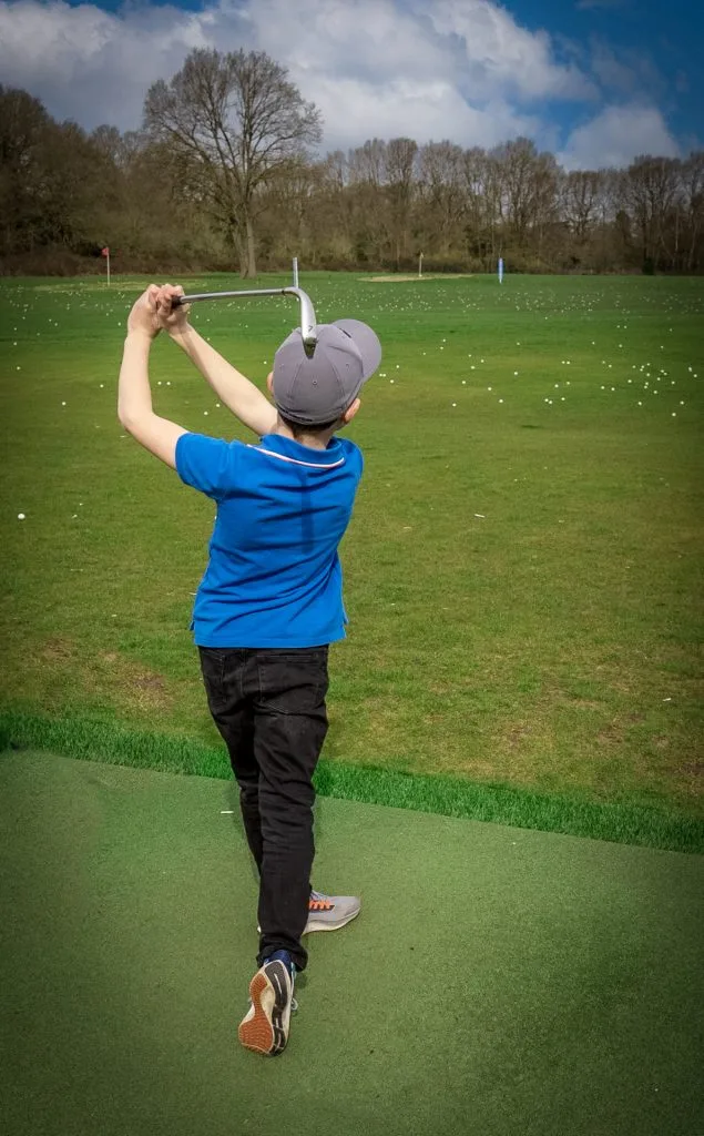 child hitting golf ball on driving range during junior golf lesson in bristol