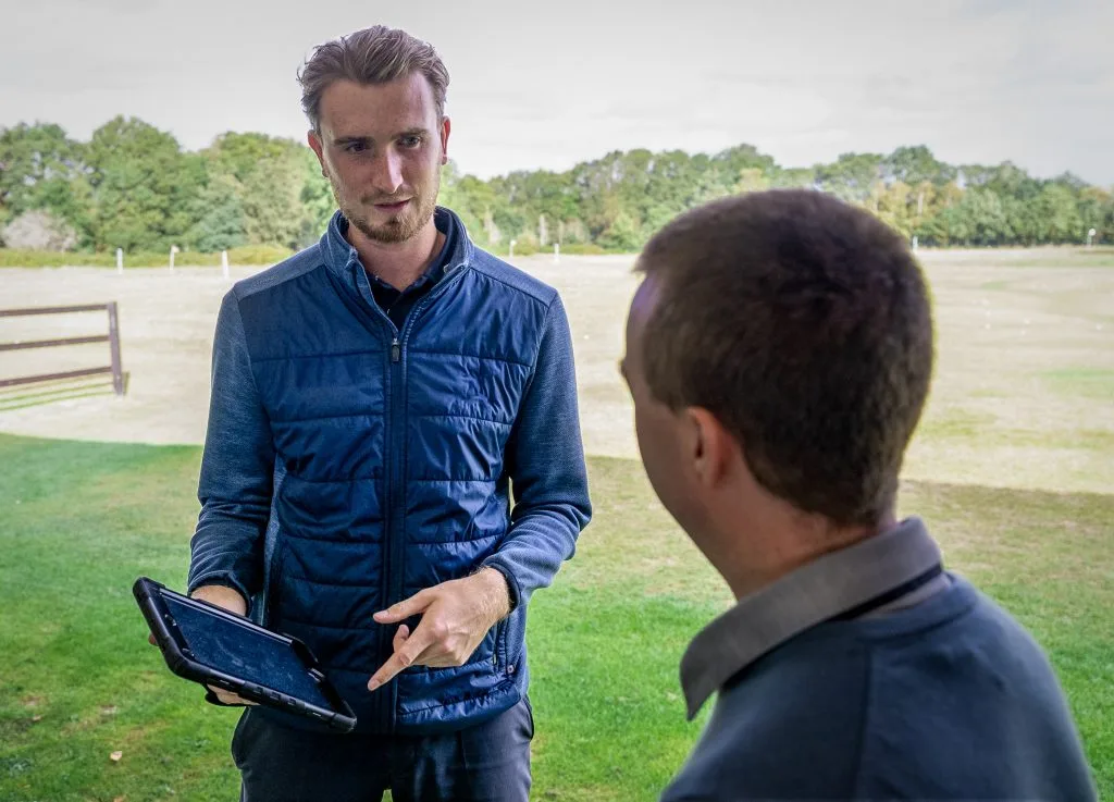 male golf pro supporting new golfer by holding ipad and showing him how to improve after golf lesson in bristol