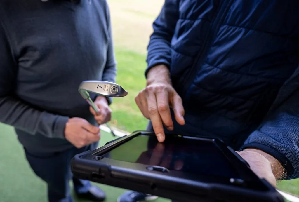 proffesional and player looking at screen to analyze after golf lessom on bristol