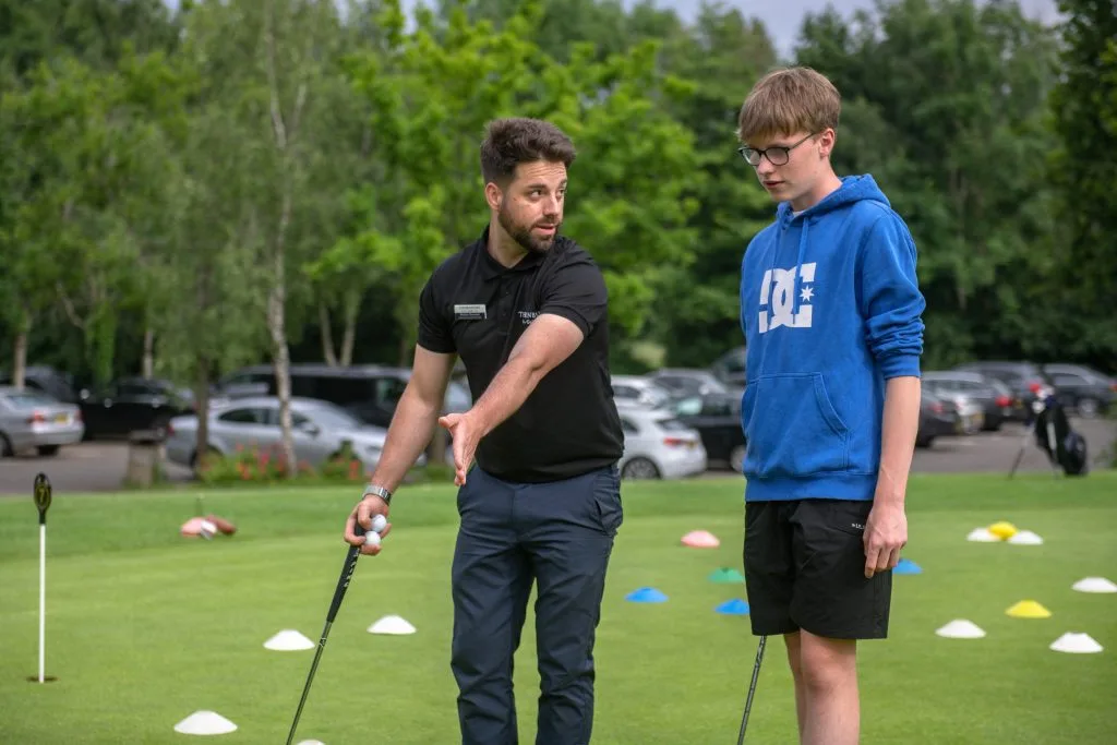 golf pro teaching young man during golf lesson
