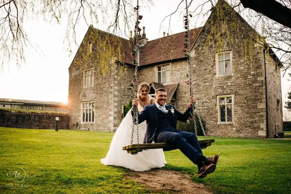 Couple sitting on a tree swing in front of Thornbury Golf and Lodge, a romantic countryside wedding venue in Bristol
