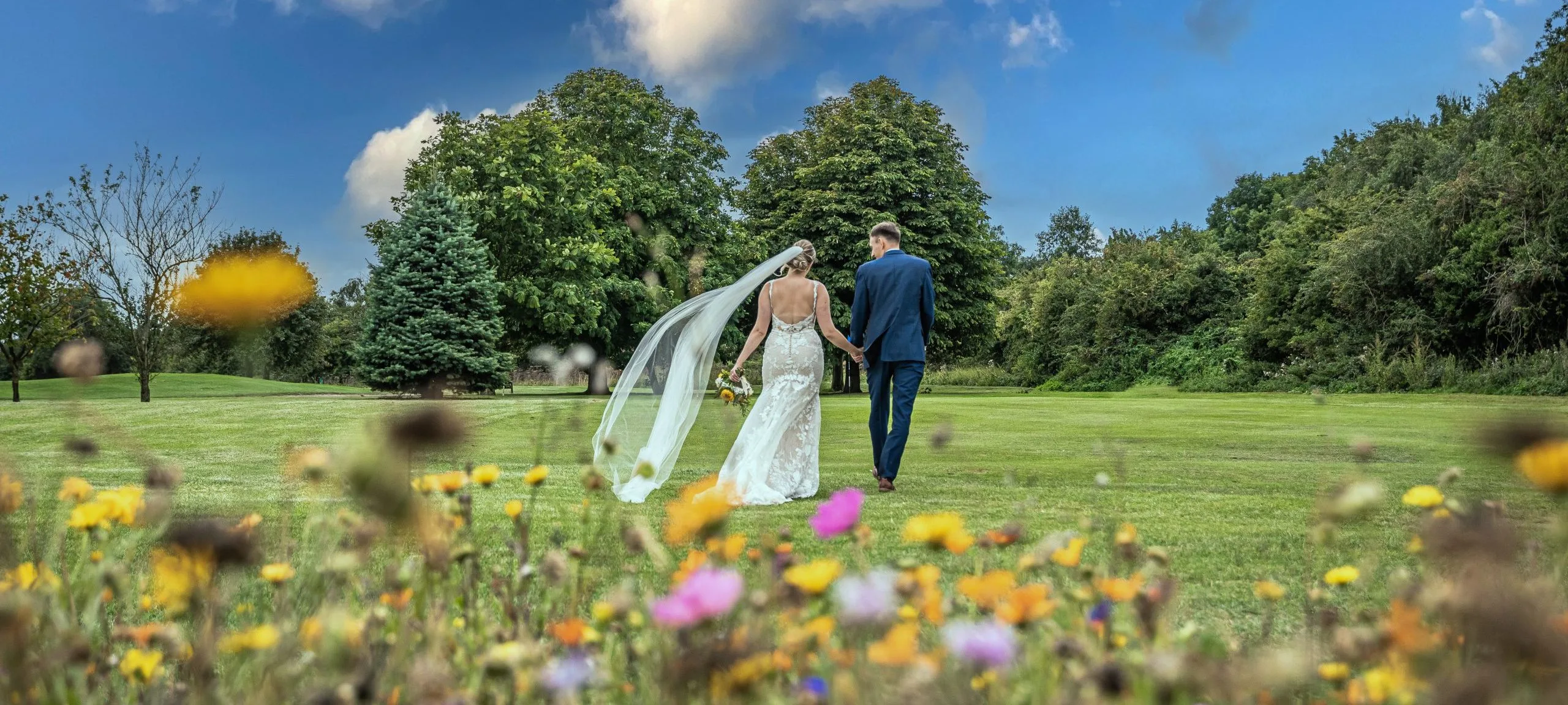 newly married couple walking in grass field covered in flowers after wedding in bristol