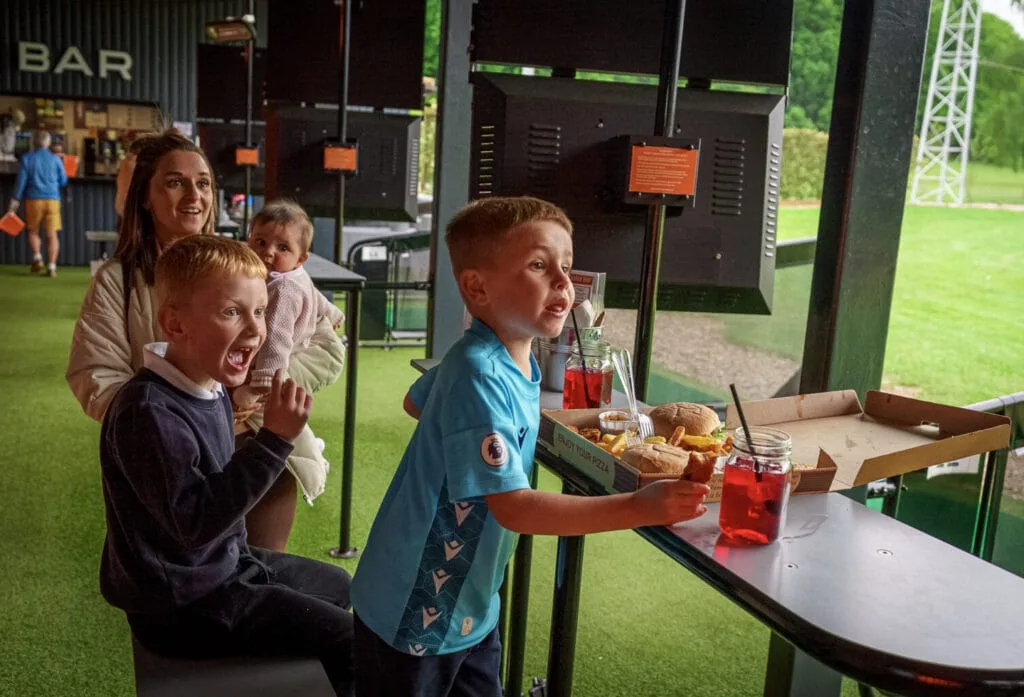 young kids playing golf on driving range and enjoying food at range bar in bristol