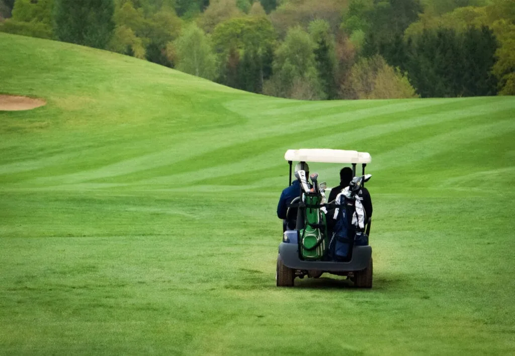 Two men driving a golf buggy across the fairway at a golf club in Bristol, enjoying golf days and using the driving range and golf shop facilities.